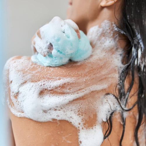 Person washing their shoulder with a blue bath loofah, shown with FinchBerry Sweet Dreams body wash